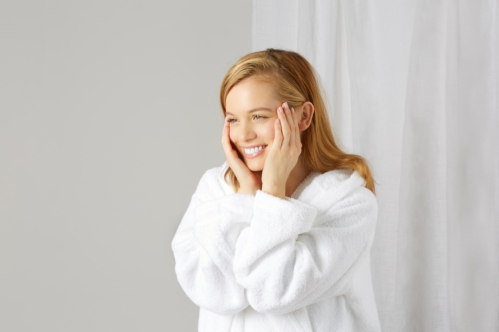 Young female model in white robe smiling and holding her face with both hands