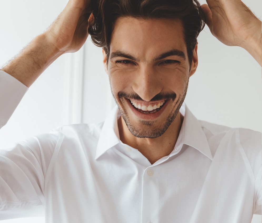 Male with a beard and moustache smiling with hands on his head