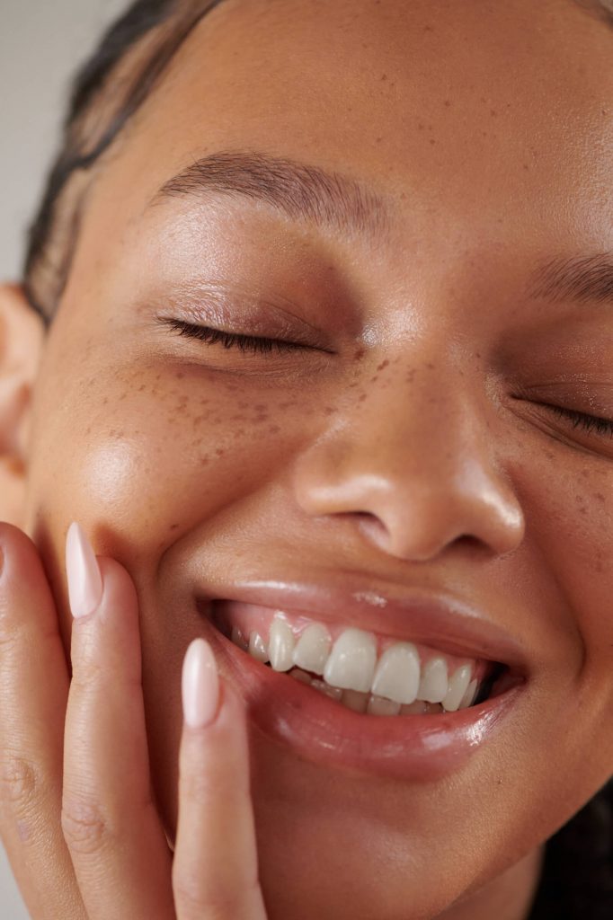 Close up of female with clear skin smiling with hand on face