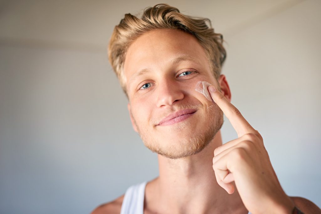 Male applying face moisturiser to cheek with one finger