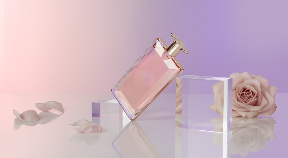 idole lancome perfume bottle balancing on glass block next to pink rose