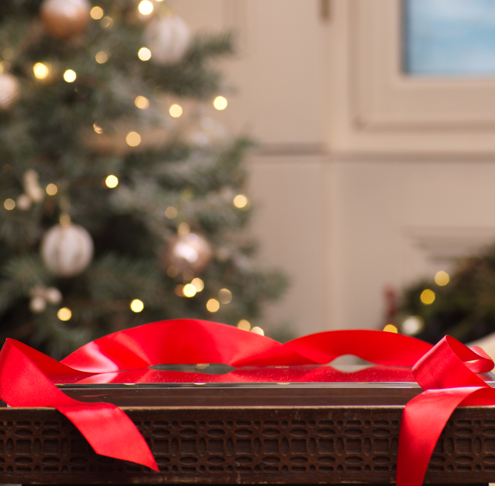 Red ribbon on top of box, Christmas tree in background