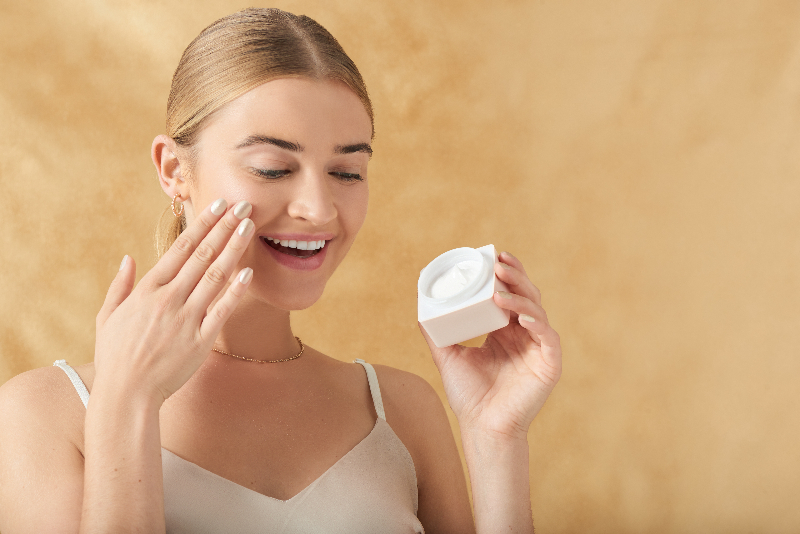 Woman applying skincare to cheek neutral background