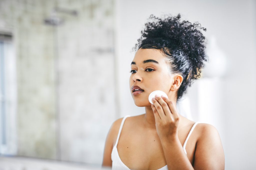 Female applying face toner with cotton pad