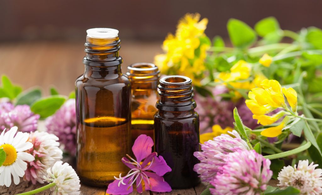 Three bottles of essential oils with flowers surrounding