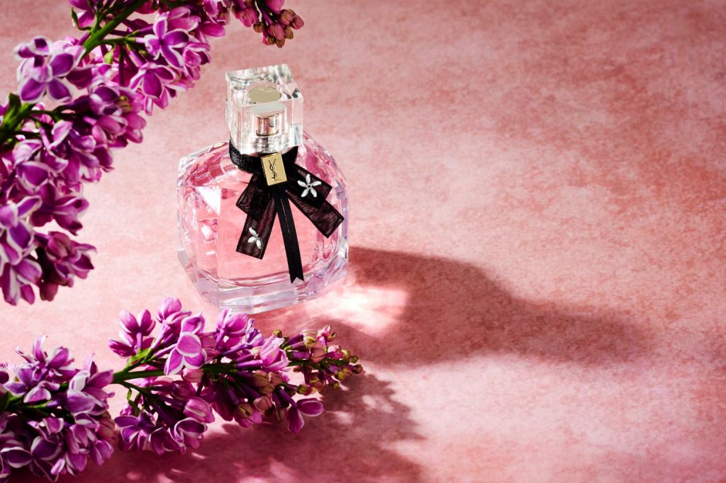 Mon Paris perfume bottle with purple flowers on pink platform