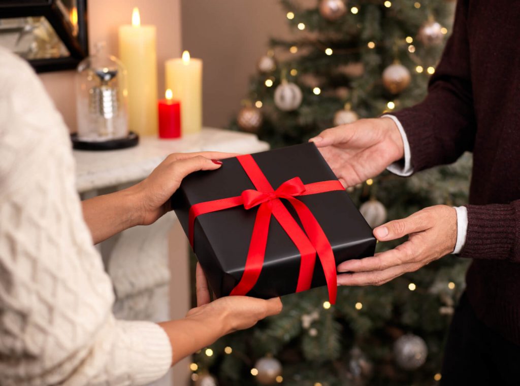 Man and woman passing Christmas gift Christmas tree in background