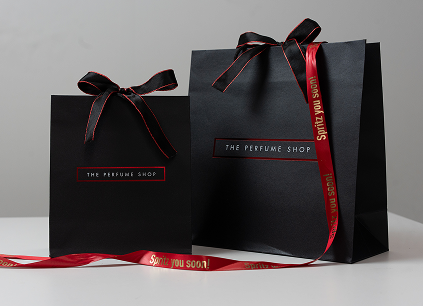 A black gift bag with The Perfume Sho logo on it and a bow