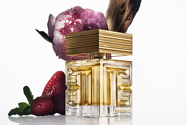 Balmain perfume bottle with gold detailing, styled with peony flower, strawberries and sandalwood to represent a floral fruity fragrance