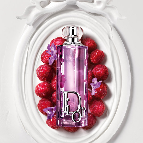 Pink Dior Addict perfume bottle displayed on a white ornate frame surrounded by pink roses.