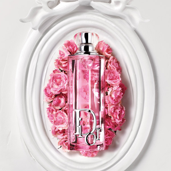Pink Dior Addict perfume bottle displayed on a white ornate frame surrounded by pink roses.