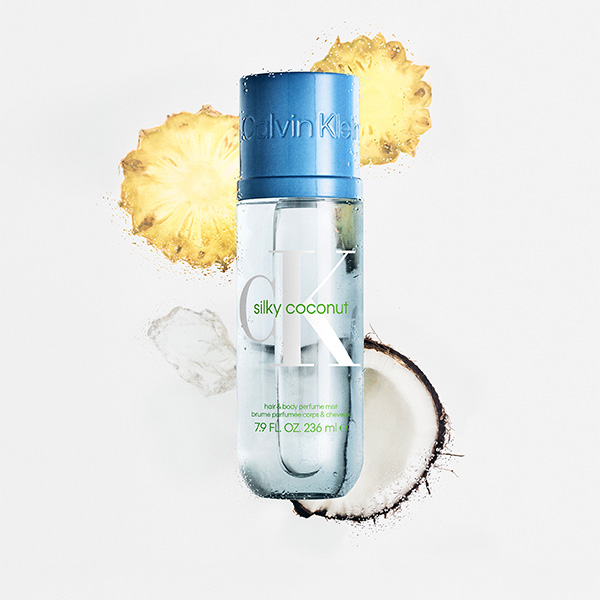 Calvin Klein CK One Silky Coconut body mist with coconut and pineapple slices on fresh backdrop