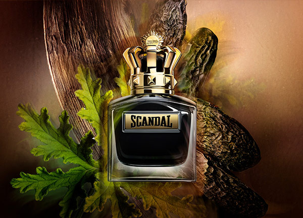Scandal perfume bottle with gold crown cap surrounded by green leaves and textured wood in a rich, earthy setting.