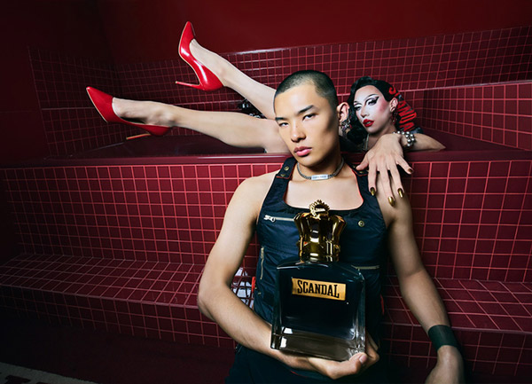 Scandal perfume bottle held in a bold red-tiled setting with striking red heels and dramatic styling elements.
