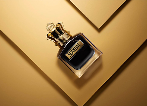 Scandal perfume bottle with gold cap on a layered gold background, luxury fragrance product shot.