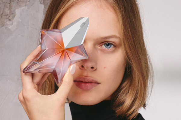 A female model holding ANgel Blush perfume bottle covering her eye