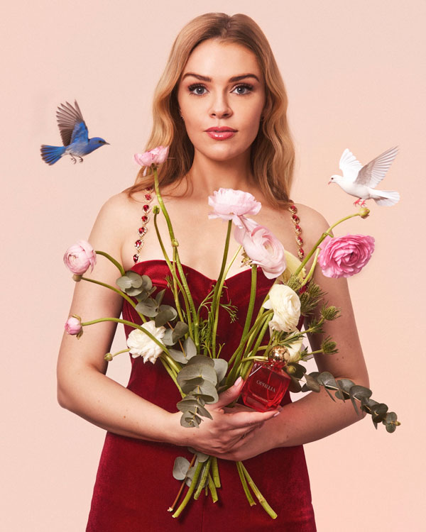 A women holding a bouquet of flowers with two birds in flight above her shoulders.